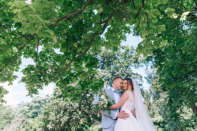 Schattige pasgetrouwden knuffelen en glimlachen in een groen park bruid en bruidegom met een lange sluier