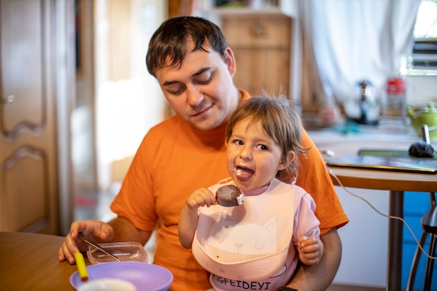 schattige peuter baby geniet van het eten van ijslolly ijs op schoot van de ouders in het interieur