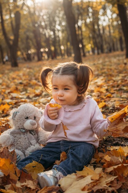 Schattige peuter babymeisje met zacht stuk speelgoed buiten spelen in herfst park klein meisje in het herfst park