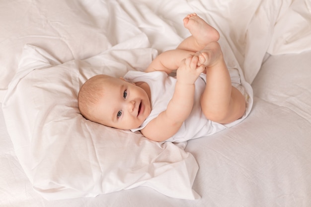 Schattige peuter in witte bodysuit ligt in bed met wit beddengoed