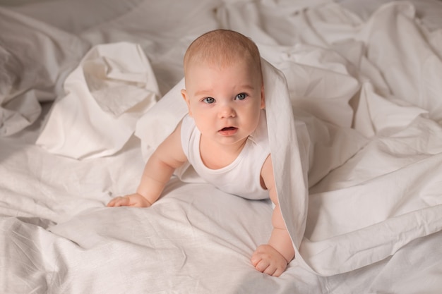 Schattige peuter in witte bodysuit ligt in bed met wit beddengoed