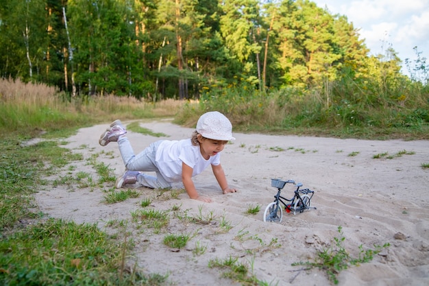 schattige peuter speelt met een speelgoedfiets in de natuur. kind op handen en voeten in het zand op het gazon.
