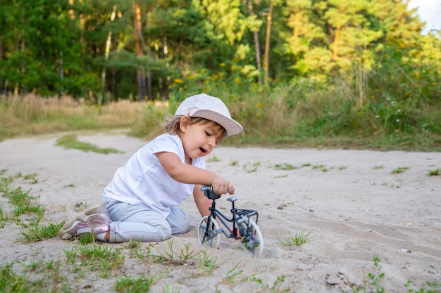 Schattige peuter speelt met een speelgoedfiets in de natuur kind op handen en voeten in het zand op het gazon