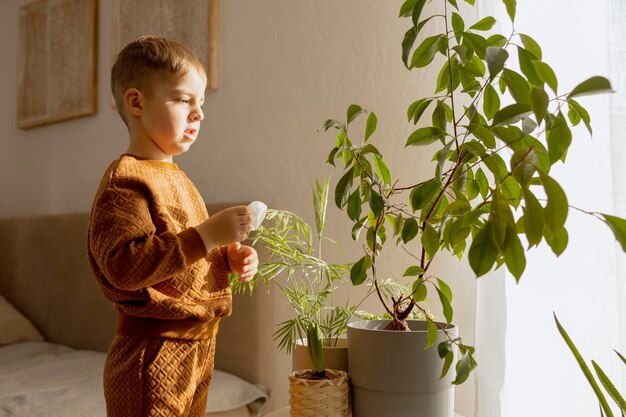 Schattige schattige jongen die thuis voor kamerplanten zorgt Een kleine helper in de huishoudelijke vrijetijdsbesteding Kind veegt stof van bladeren Huis tuinieren concept Gezellige kamer aardekleuren Vrijetijdskleding