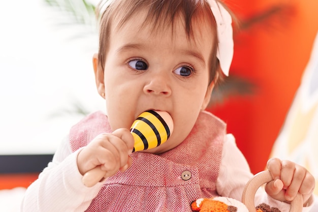 Schattige Spaanse baby die maraca op bed in de slaapkamer zit