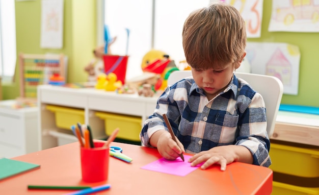 Schattige Spaanse jongen preschool student zittend op tafel tekenen op papier op de kleuterschool