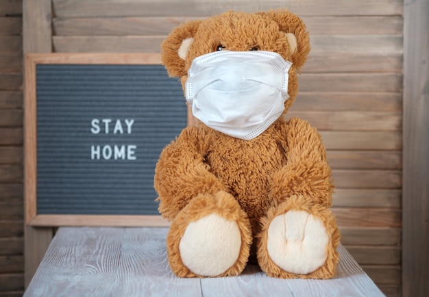 Schattige teddybeer in een medisch masker op een grijs viltbordje met de tekst blijf thuis. concept van thuisquarantaine tijdens de covid-19 coronavirus-pandemie