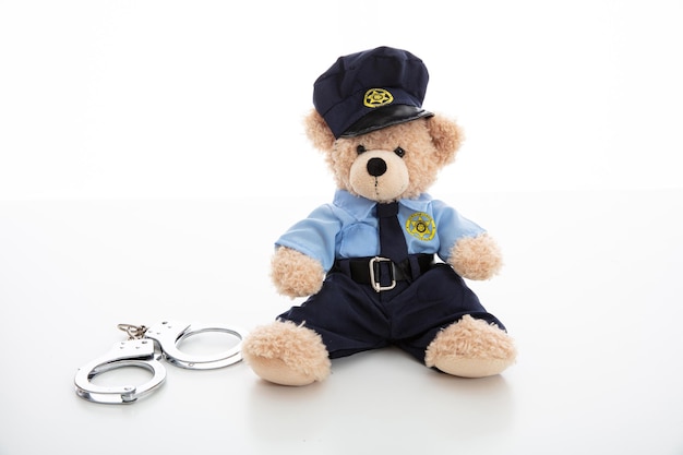 Schattige teddybeer in politieagent uniform en handboeien geïsoleerd tegen een witte achtergrond