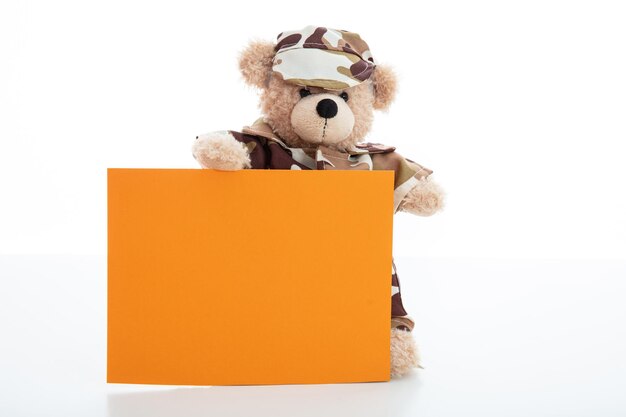 Schattige teddybeer in soldatenuniform en een lege oranje kleurenkaart geïsoleerd tegen een witte achtergrond