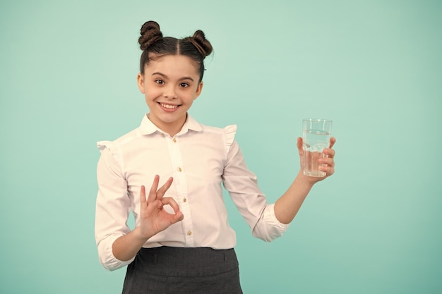 Schattige tiener meisje drinkwater uit glas op blauwe achtergrond Gelukkig tiener positieve en lachende emoties van tiener meisje