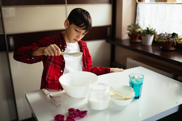 Schattige tienerjongen van 11 jaar mix ingrediënten voor deeg, kook thuis, gepassioneerd door bakken, hobby, koken voor kinderen, levensstijl