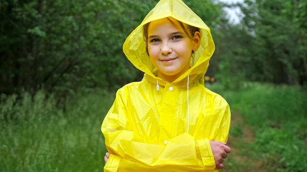 Schattige tienermeisje in gele regenjas kijkt glimlachend in de camera