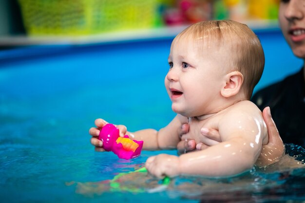 schattige trieste babyjongen die leert zwemmen in een speciaal zwembad voor kleine kinderen