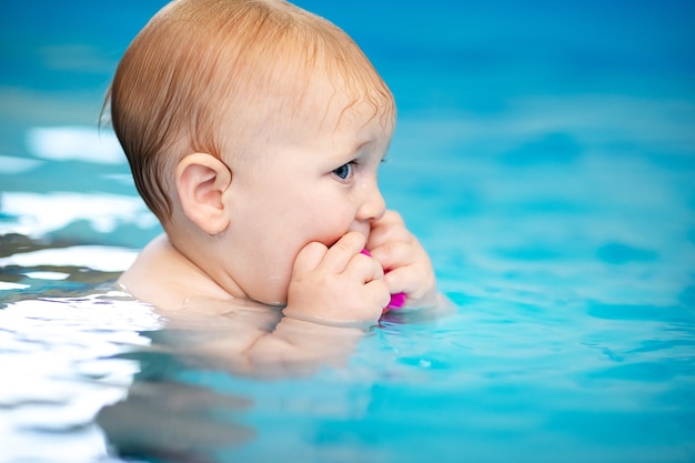 schattige trieste babyjongen die leert zwemmen in een speciaal zwembad voor kleine kinderen