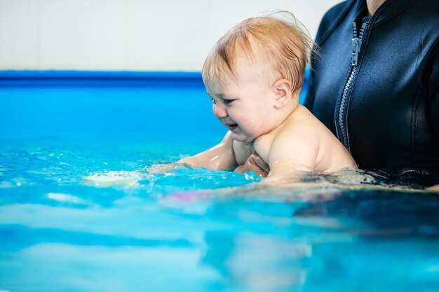 schattige trieste babyjongen die leert zwemmen in een speciaal zwembad voor kleine kinderen