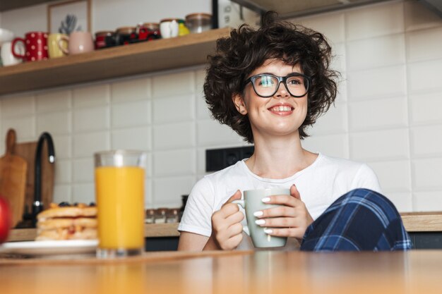 schattige vrij krullend vrouw zitten aan de keuken het drinken van thee