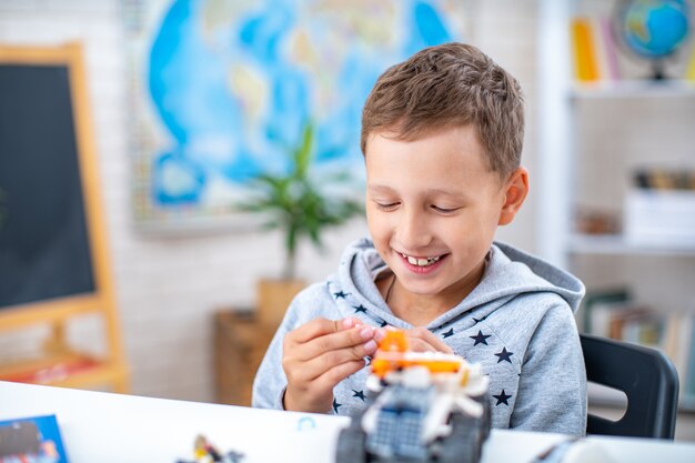 Schattige zevenjarige jongen, schooljongen, heeft plezier met constructeur, zittend aan tafel