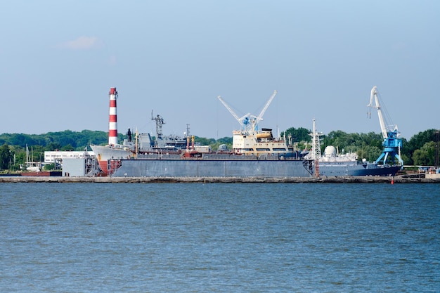 Scheepswerf voor reparatie- en onderhoudsschepen, revisie van vrachtschepen in reparatiedok. Dockyard aan het werk. Industriële machines en kranen. Vervoer, vrachtconcept. Blauwe lucht en zee, zonnige dag