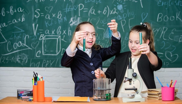 Scheikunde studeren interessant maken Educatief experimentconcept Meisjes klasgenoten studeren scheikunde Microscoop en reageerbuisjes op tafel Chemische reacties uitvoeren Basiskennis van scheikunde