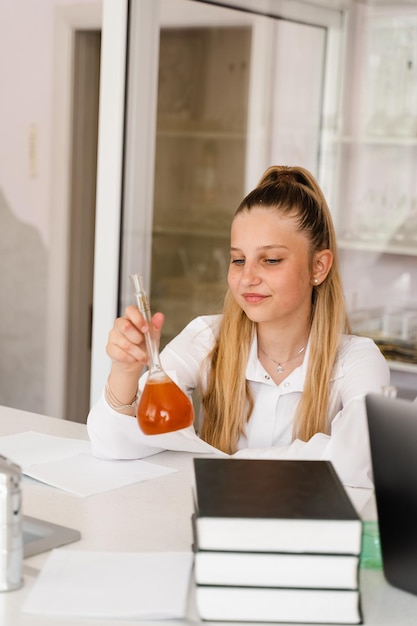 Scheikundeles op school Meisje met kolf studeert in scheikundeklas Schoolmeisje met kolf met chemische stof in het laboratorium