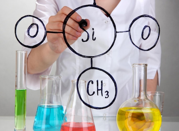 Scheikundige vrouw formules schrijven op glas op grijze achtergrond