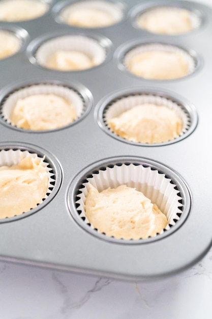 Schep cupcakebeslag in een met cupcakevormpjes beklede cupcakevorm om vanillecupcakes te bakken.