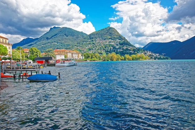 Schepen bij de aanlegsteiger aan de promenade van het luxe resort in Lugano aan het meer van Lugano en de Alpen in het kanton Ticino in Zwitserland.