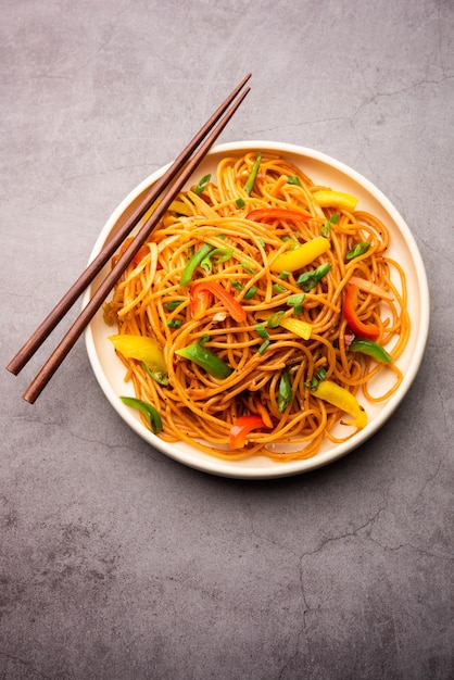 Schezwan noodles or szechwan vegetable hakka noodles or chow\
mein is a popular indo-chinese recipes, served in a bowl or plate\
with wooden chopsticks