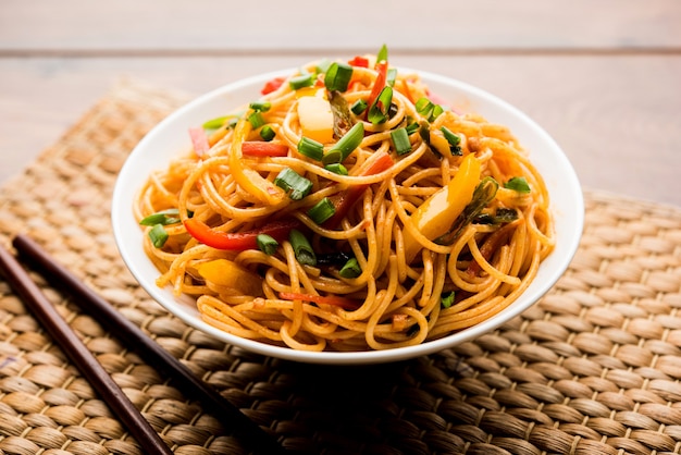 Foto schezwan noodles o verdure hakka noodles o chow mein è una popolare ricetta indo-cinese, servita in una ciotola o in un piatto con bacchette di legno. messa a fuoco selettiva