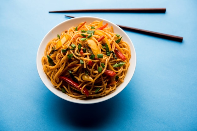 Schezwan Noodles or vegetable Hakka Noodles or chow mein is a popular Indo-Chinese recipes, served in a bowl or plate with wooden chopsticks. selective focus