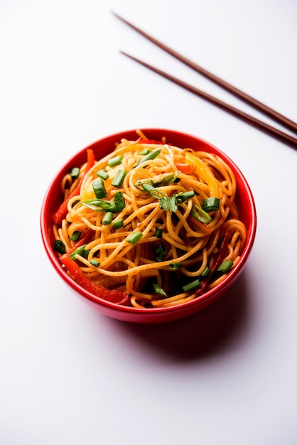 Schezwan Noodles or vegetable Hakka Noodles or chow mein is a popular Indo-Chinese recipes, served in a bowl or plate with wooden chopsticks. selective focus