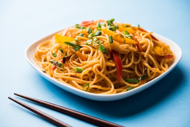Schezwan Noodles or vegetable Hakka Noodles or chow mein is a popular Indo-Chinese recipes, served in a bowl or plate with wooden chopsticks
