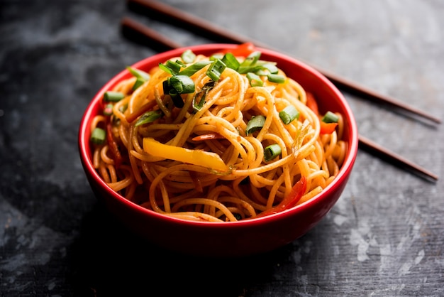 Schezwan Noodles or vegetable Hakka Noodles or chow mein is a popular Indo-Chinese recipes, served in a bowl or plate with wooden chopsticks