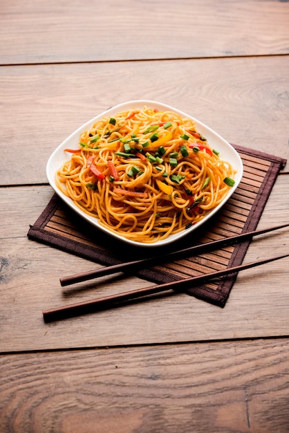 Schezwan Noodles or vegetable Hakka Noodles or chow mein is a popular Indo-Chinese recipes, served in a bowl or plate with wooden chopsticks