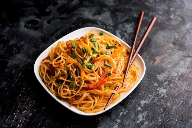 Schezwan Noodles or vegetable Hakka Noodles or chow mein is a popular Indo-Chinese recipes, served in a bowl or plate with wooden chopsticks