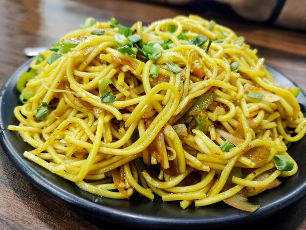 Schezwan noodles or vegetable hakka noodles or chow mein with corn and tomato served in a plate on wooden table selective focus