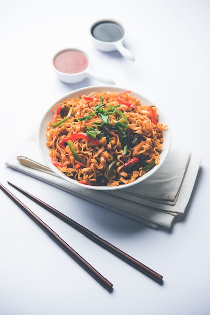 Schezwan veg noodles is a spicy and tasty stir fried flat Hakka noodles with sauce and veggies. served with chopsticks. selective focus