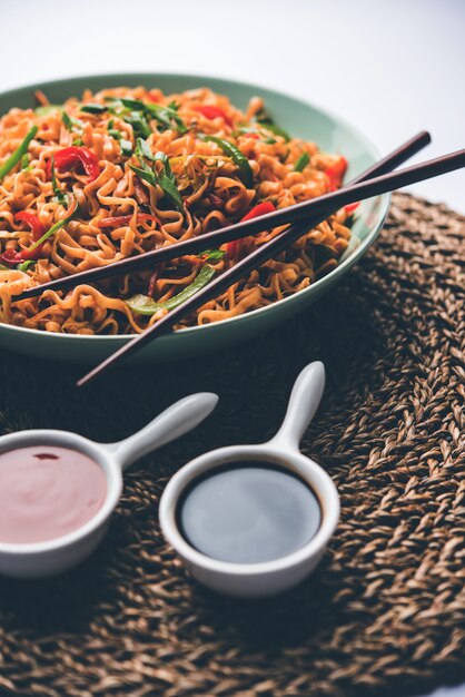 Schezwan veg noodles is a spicy and tasty stir fried flat Hakka noodles with sauce and veggies. served with chopsticks. selective focus