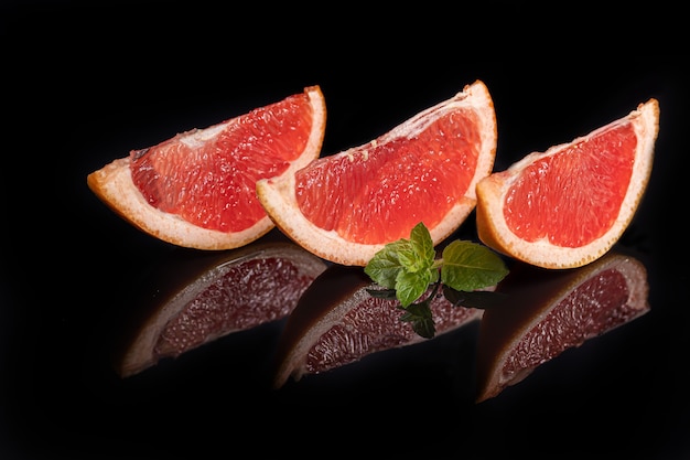 Schijfjes grapefruit op een donkere achtergrond met een takje munt. Isoleren. Ruimte kopiëren.