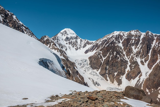 Schilderachtig alpenlandschap met besneeuwde bergtop en steile gletsjertong met ijsval in zonlicht Geweldig berglandschap met puntige piek en gletsjer op rotsen onder blauwe lucht op zonnige dag