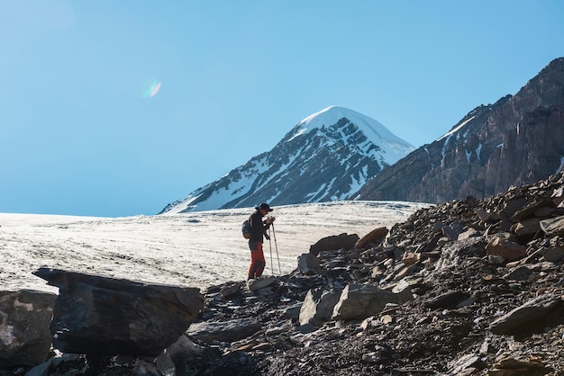 Schilderachtig alpenlandschap met silhouet van wandelaar met wandelstokken tegen grote gletsjertong en besneeuwde bergtop in zonlicht Man met rugzak in hoge bergen onder blauwe lucht op zonnige dag