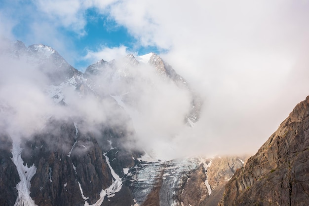 Schilderachtig berglandschap met besneeuwde bergtop en gletsjer in dichte lage wolken in zonsopgangkleuren Kleurrijk uitzicht op de bergen naar verticale gletsjer met ijsval in ochtendzonlicht in dikke lage wolken