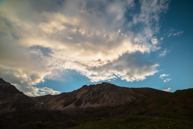 Schilderachtig landschap met een donker silhouet van een bergketen onder een avondblauwe hemel met oranje zonsondergangwolken Zonovergoten oranje cirruswolken in zonsonderganghemel boven silhouet van bergtop bij wisselvallig weer