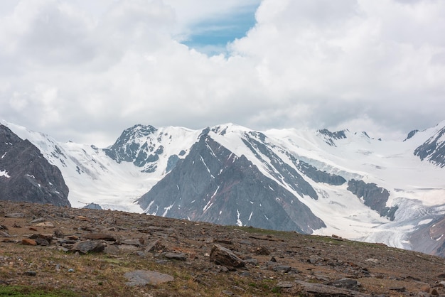 Schilderachtig landschap met hoge besneeuwde bergketen en lange gletsjertong in zonlicht onder bewolkte hemel Geweldig alpenzicht op zonovergoten grote sneeuwbergen onder wolken in blauwe hemel bij veranderlijk weer