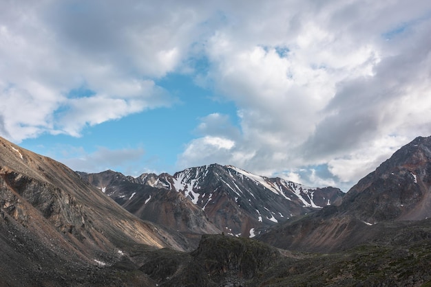 Schilderachtig landschap met hoge sneeuwberg met scherpe rotsachtige top in zonlicht onder wolken in blauwe lucht bij veranderlijk weer Kleurrijk berglandschap tot zonovergoten grote bergtop onder bewolkte hemel