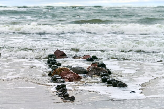 Schilderachtig uitzicht op de blauwe zee met schuimende golven. vintage lange houten golfbrekers die zich uitstrekken tot ver naar de zee, winterlandschap van de oostzee. stilte, eenzaamheid, rust en vrede.