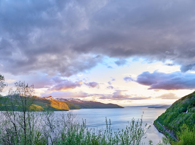 Schilderachtig uitzicht op een meer, oceaan of zee met bewolkte lucht bij zonsondergang en kopieer ruimteOngecultiveerde bomen struiken struiken rond een baai van water in Noorwegen Landschap van kalme serene vredige rustige natuurvijver