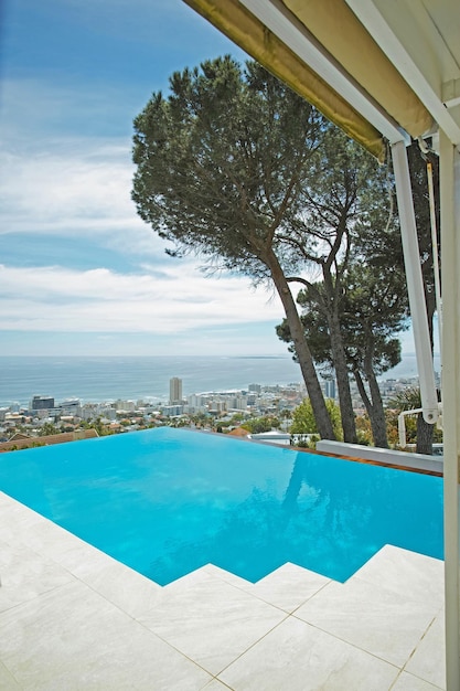 Schilderachtig uitzicht op het oneindige zwembad met uitzicht op de stad en de oceaan op de achtergrond Luxe blauw buitenzwembad op een betegeld terras en veranda van een condo-huis of hotel Stadsgezicht en skyline met zee