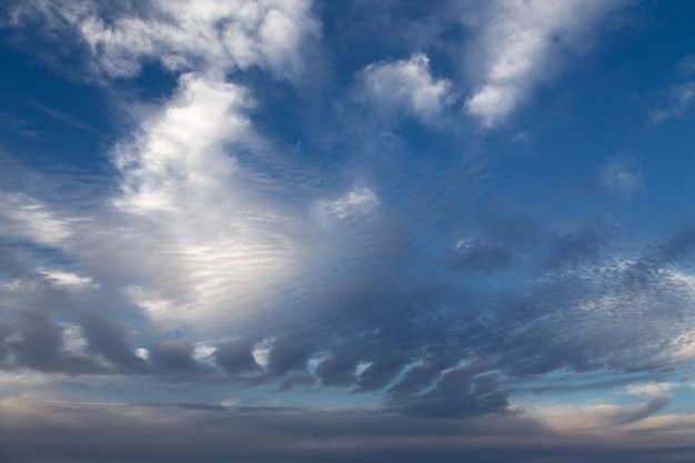 Schilderachtige cloudscape-achtergrond met licht getextureerde wolken op een donkerblauwe lucht