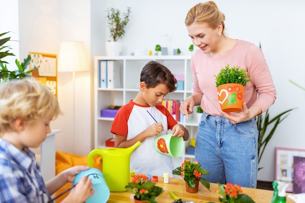 Schildertijd. Blondharige, stralende ecologieleraar kijkt toe hoe haar schattige leerlingen bloempotten kleuren